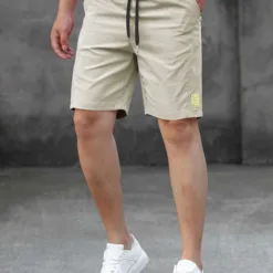 A man wearing a pair of beige men's tech shorts with a black drawstring.