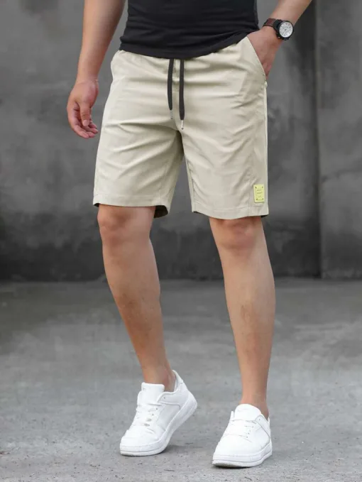 A man wearing a pair of beige men's tech shorts with a black drawstring.