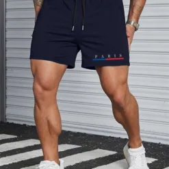 A man with a muscular physique wearing a pair of navy blue men's athletic shorts with a 'Paris' graphic.
