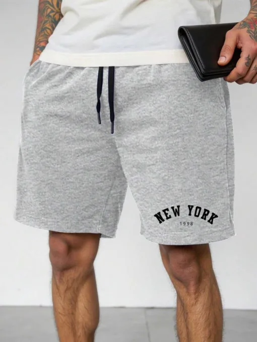 A man wearing a pair of heather grey men's sweat shorts with a 'New York 1998' graphic.