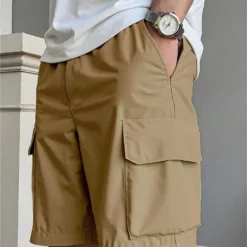 A man wearing a pair of modern, khaki men's cargo shorts with a clean side pocket.