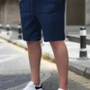 A man wearing a pair of navy blue men's chino shorts with a drawstring waist and white sneakers.