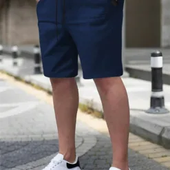 A man wearing a pair of navy blue men's chino shorts with a drawstring waist and white sneakers.