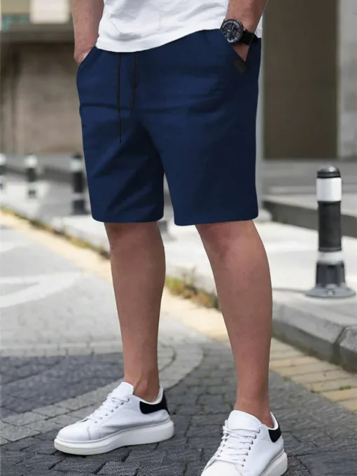 A man wearing a pair of navy blue men's chino shorts with a drawstring waist and white sneakers.