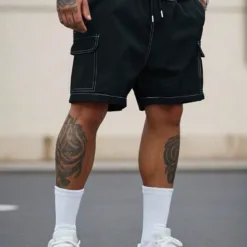 A man wearing black men's cargo shorts with white contrast stitching and white sneakers.