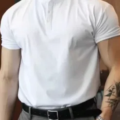 A man wearing a white slim fit men's Henley shirt with grey trousers.